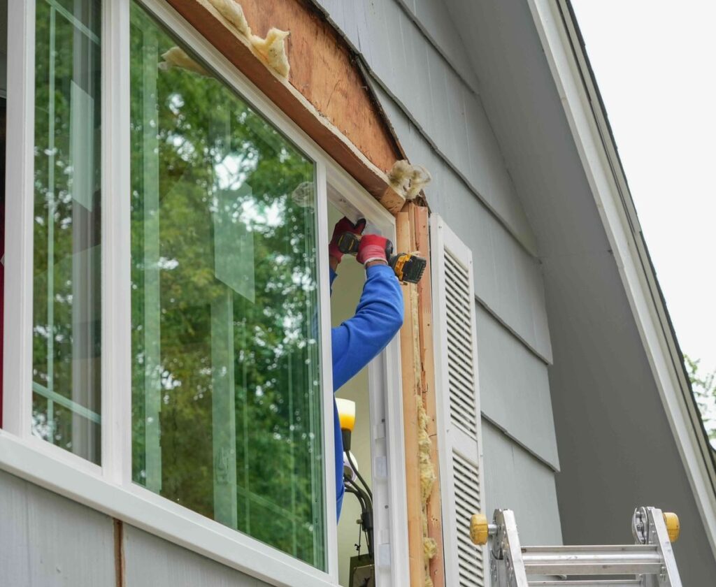 Worker installing a new window on a house exterior.