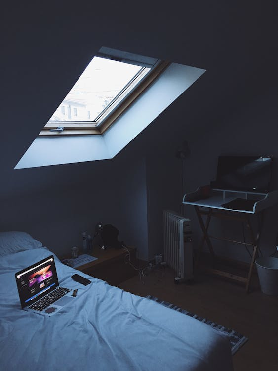 Cozy attic bedroom with skylight, bed, and laptop