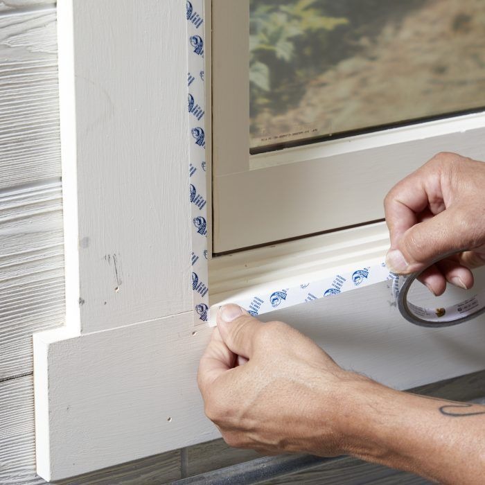 Applying weather stripping tape around a window for sealing.